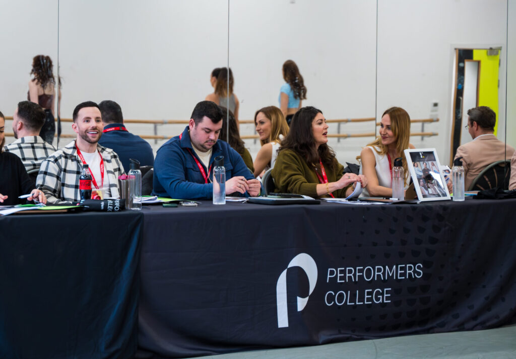 A row of agents watch performers college students dance in an audition