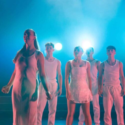 A group of dancers in elegant white dresses performing gracefully on stage, showcasing their synchronized movements.